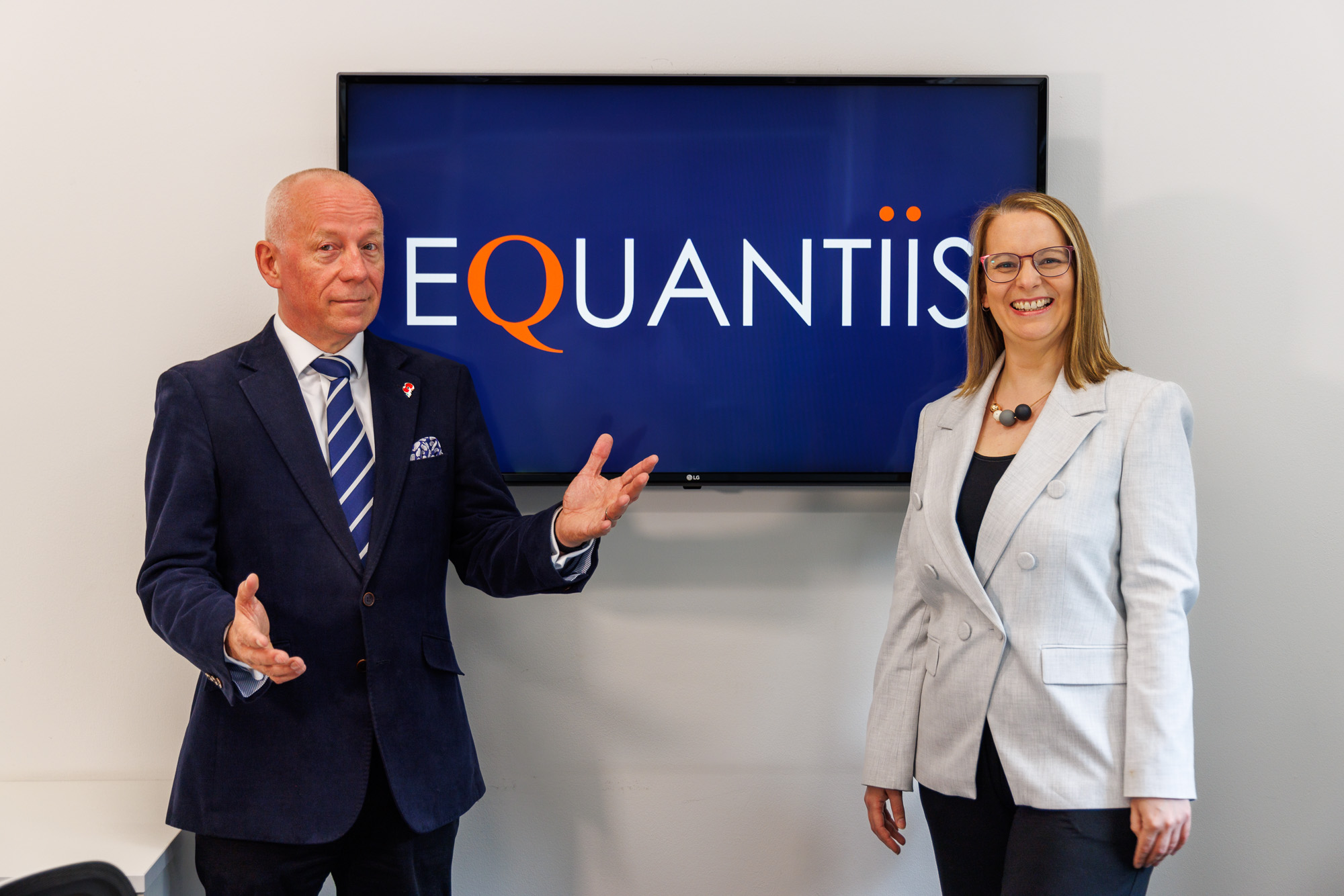 two equantiis consultants standing next to a tv with company logo on screen