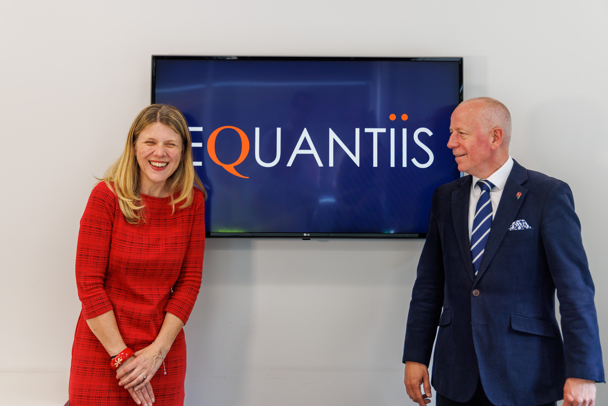 equantiis consultants standing next to a tv with company logo on screen